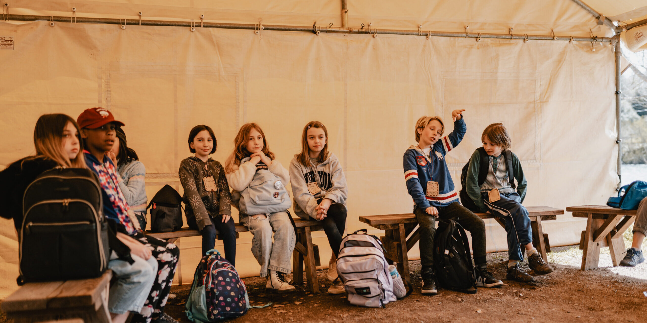 kids sitting on bench inside of tent with their bags